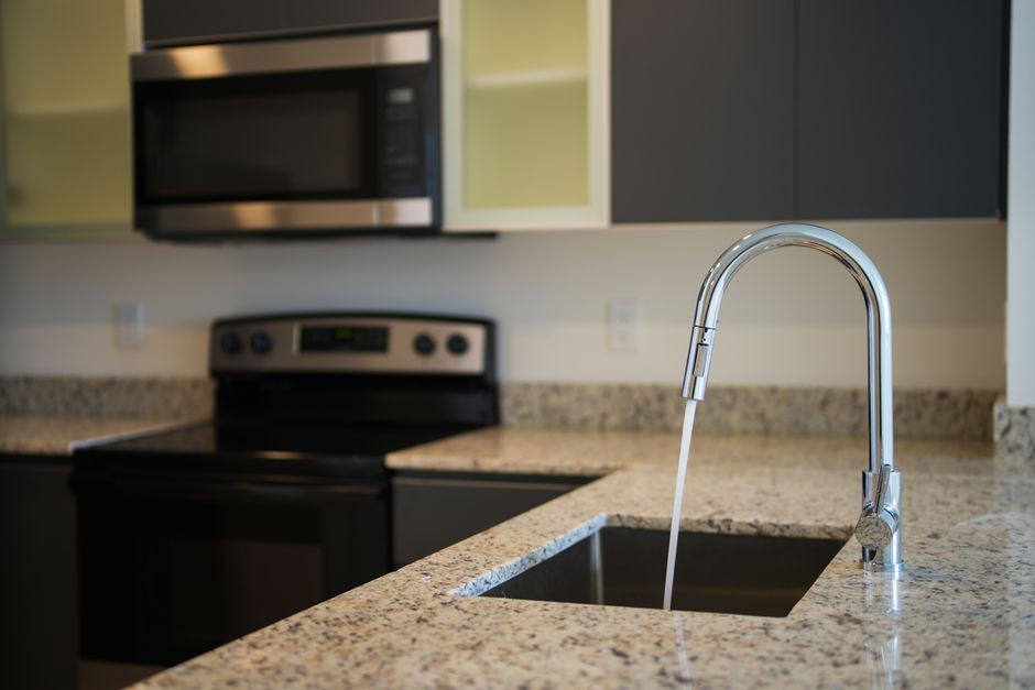 A sleek kitchen faucet on a granite countertop with modern appliances in view.