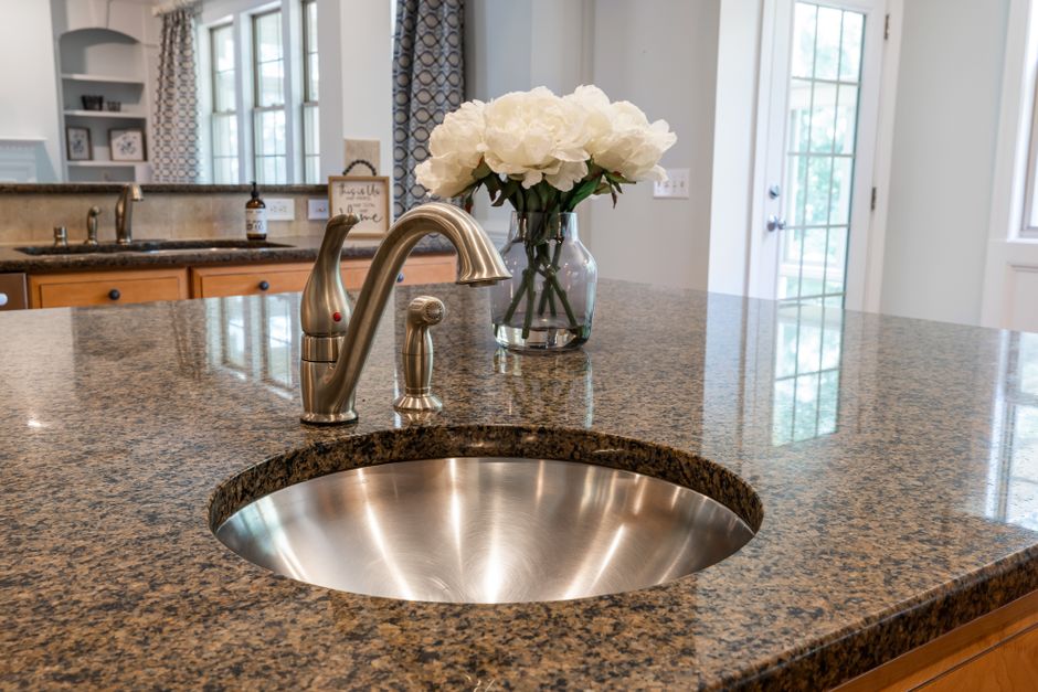 Stylish kitchen interior featuring granite countertop, stainless steel sink, and a vase of white peonies.