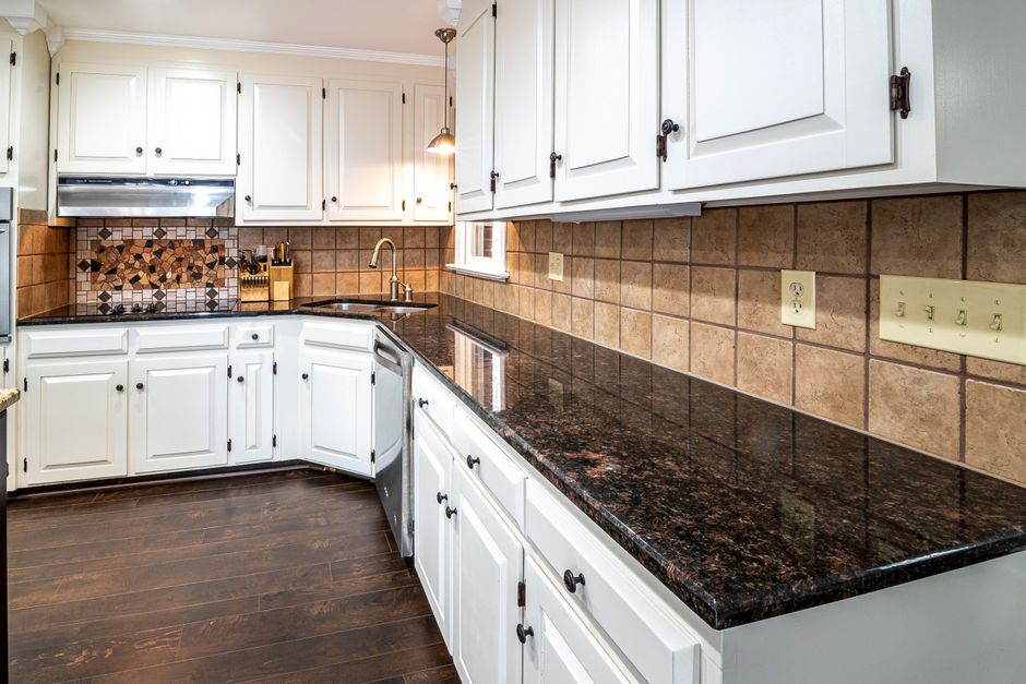 Stylish kitchen featuring granite countertops, white cabinets, and a tiled backsplash